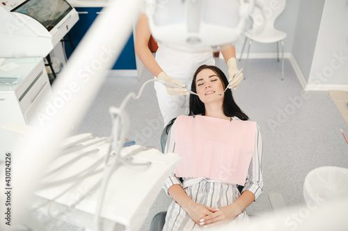 Image of pretty young woman sitting in dental chair at medical center while professional doctor fixing her teeth