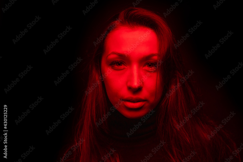 Young pretty woman looks at camera in contrast red light. Sensual female person posing in dark studio with red neon lightning. Portrait of beautiful sexy woman, art fashion beauty concept Young pretty woman looks at camera in contrast red light. Sensual female person posing in dark studio with red neon lightning. Portrait of beautiful sexy woman, art fashion beauty concept