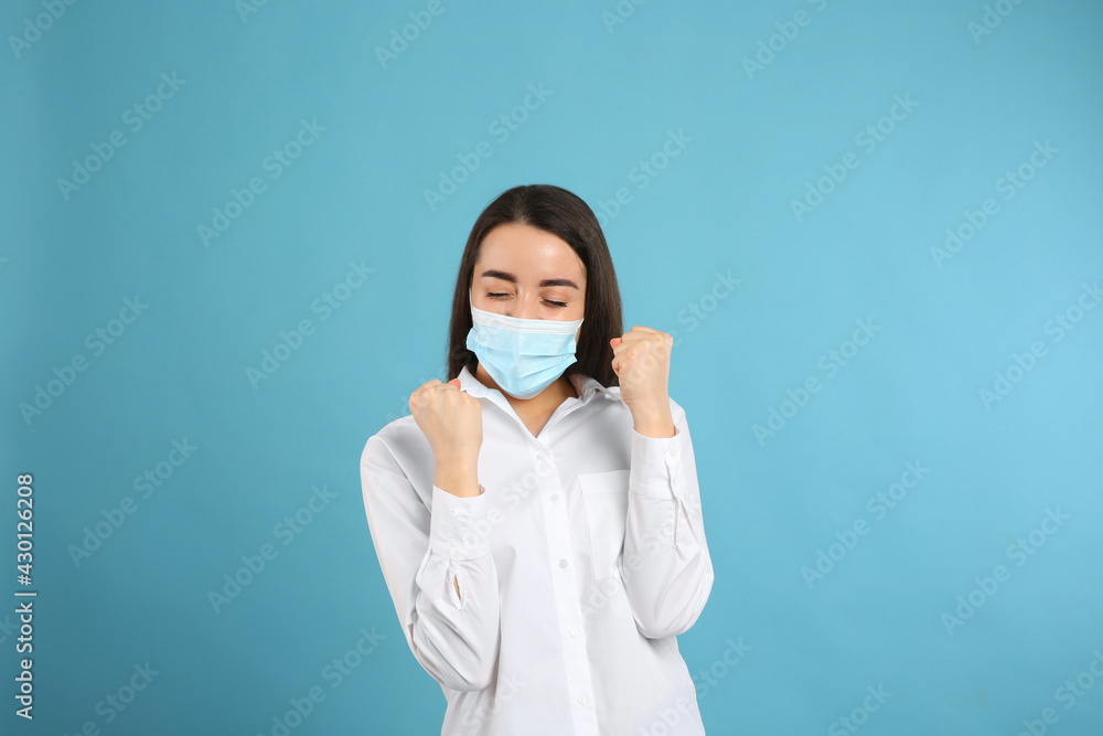 Emotional woman with protective mask on light blue background. Strong immunity concept