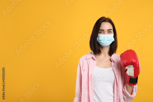 Woman with protective mask and boxing gloves on yellow background  space for text. Strong immunity concept