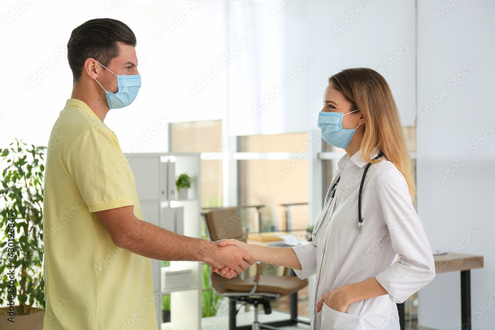 Doctor and patient in protective masks shaking hands indoors Doctor and patient in protective masks shaking hands indoors