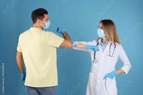 Doctor and patient doing elbow bump instead of handshake on light blue background. New greeting during COVID-19 pandemic