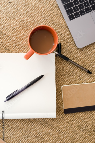 Cup of coffee with notebooks, ballpens, and laptop on brown burlap textile photo