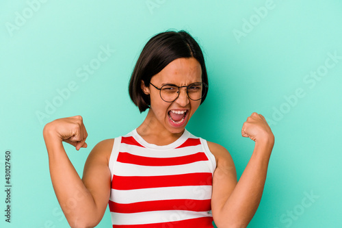 Young mixed race woman isolated on blue background showing strength gesture with arms, symbol of feminine power