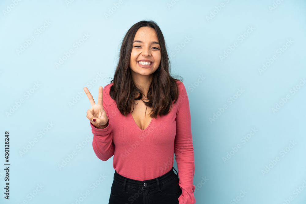 Young mixed race woman isolated on blue background smiling and showing victory sign Young mixed race woman isolated on blue background smiling and showing victory sign