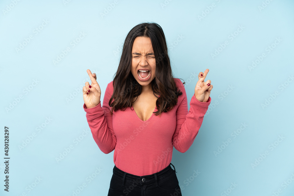Young mixed race woman isolated on blue background with fingers crossing Young mixed race woman isolated on blue background with fingers crossing