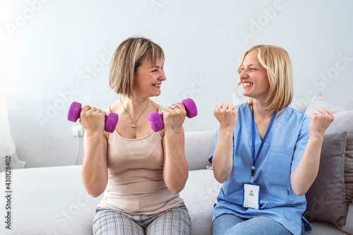 Physical Injury Recovery. Nurse home visiting a patient, showing her exercises for arms strength. Candid image of an attractive patient during a appointment with professional physiotherapist at home