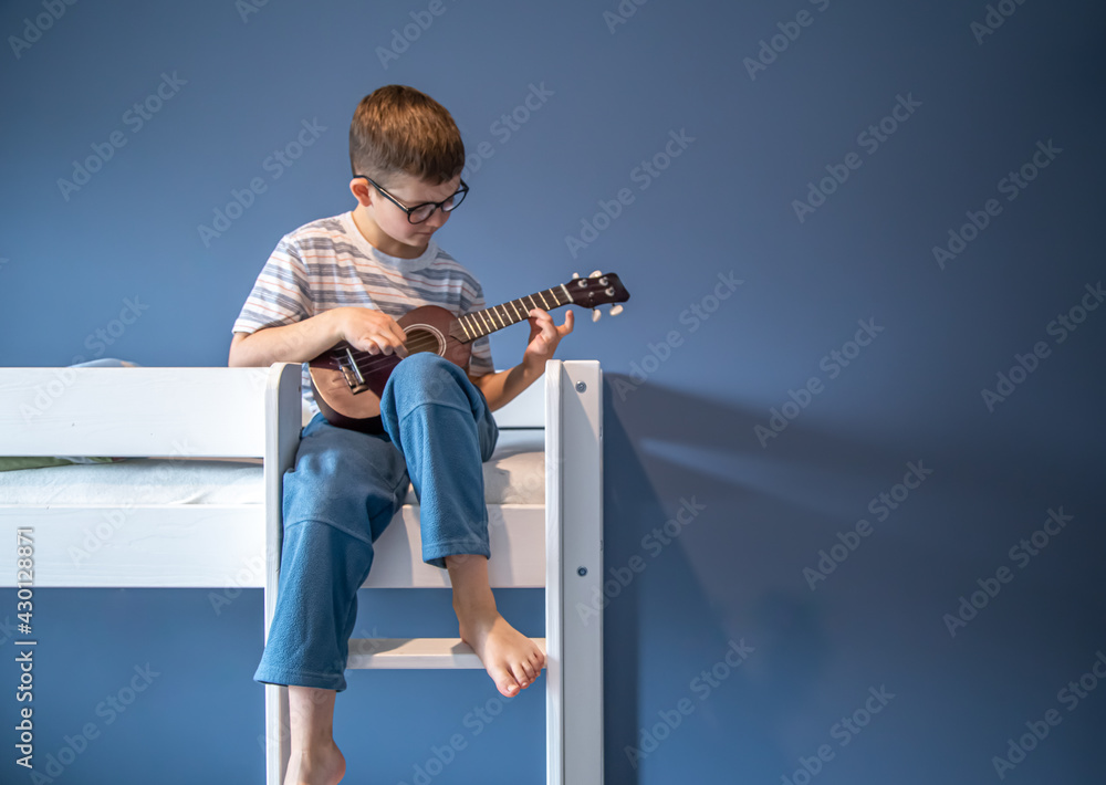 Little boy playing ukulele sitting on the bed at home copy space. Little boy playing ukulele sitting on the bed at home copy space.