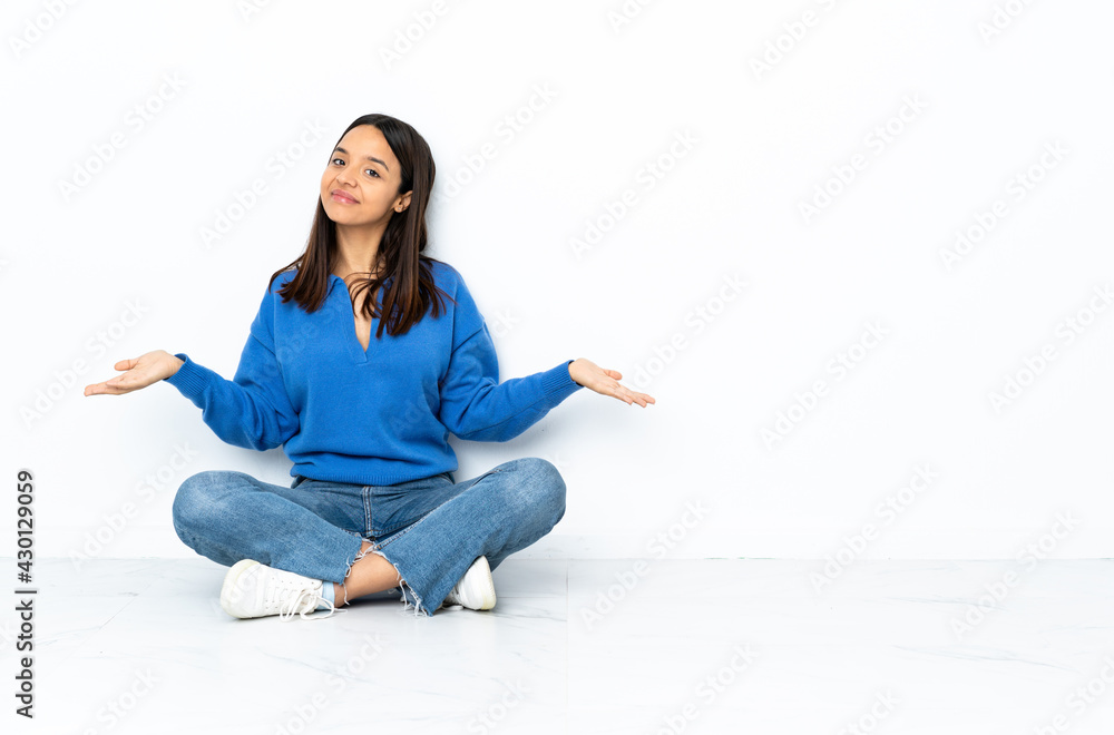 Young mixed race woman sitting on the floor isolated on white background having doubts Young mixed race woman sitting on the floor isolated on white background having doubts