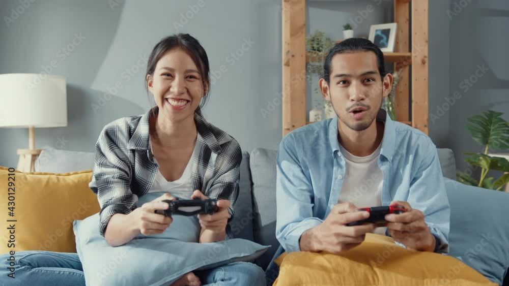 Happy asia young couple man and woman sit on couch use joystick controller play video game spend fun time together in living room. Asian married couple family lifestyle, Couple stay at home concept. Happy asia young couple man and woman sit on couch use joystick controller play video game spend fun time together in living room. Asian married couple family lifestyle, Couple stay at home concept.