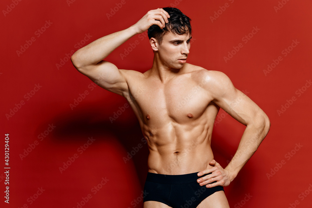 Fototapeta premium guy in black shorts holds his hand on his head on a red background pose model torso