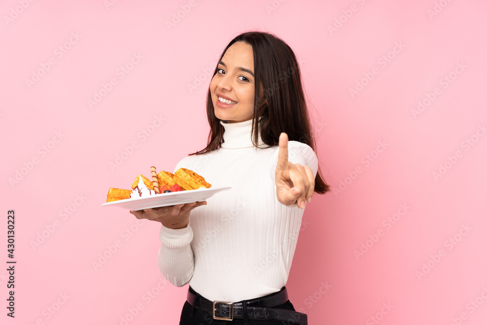 Young brunette woman holding waffles over isolated pink background showing and lifting a finger Young brunette woman holding waffles over isolated pink background showing and lifting a finger