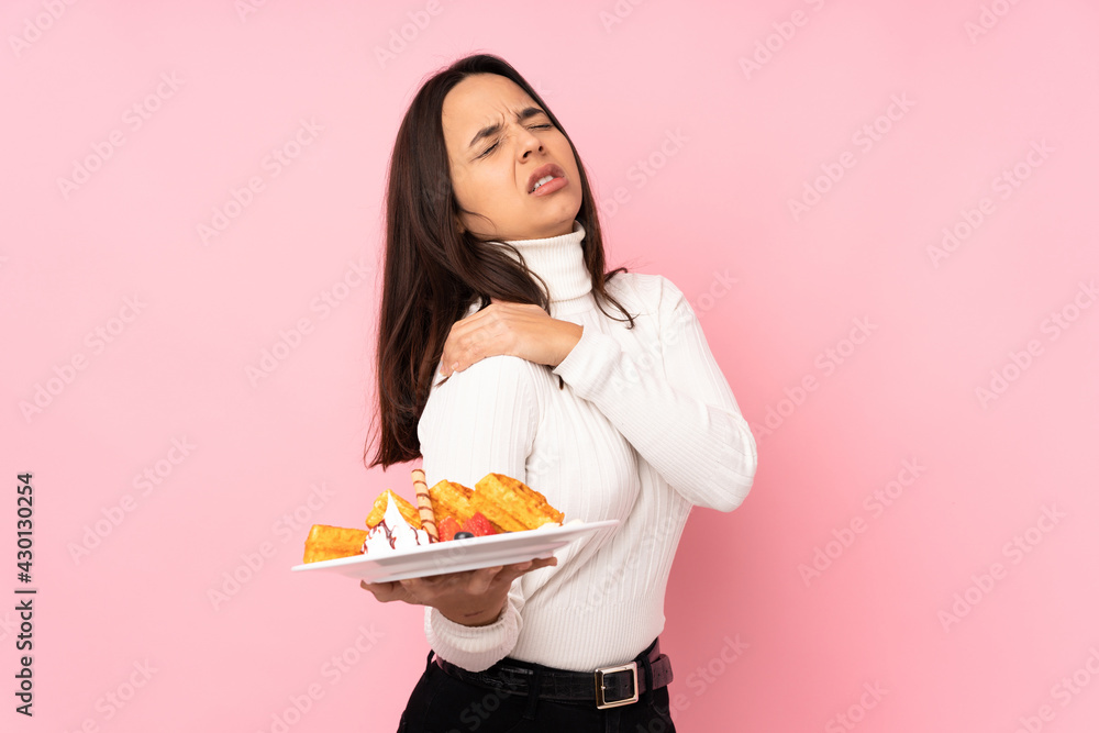 Young brunette woman holding waffles over isolated pink background suffering from pain in shoulder for having made an effort Young brunette woman holding waffles over isolated pink background suffering from pain in shoulder for having made an effort