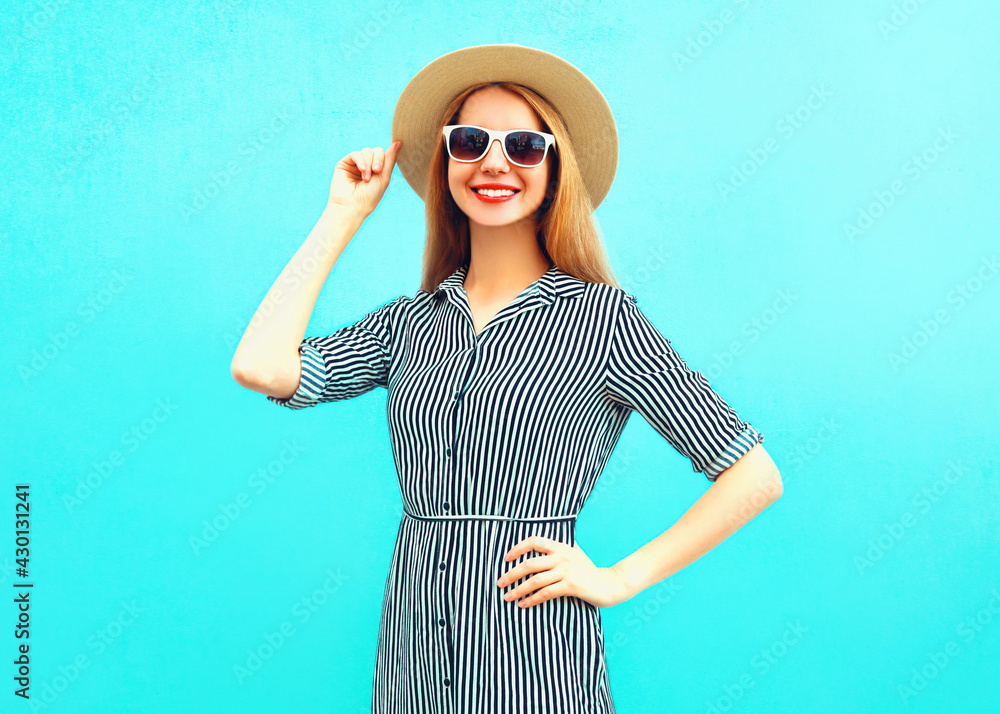 Portrait of happy smiling young woman wearing a summer straw hat, striped dress on a blue background Portrait of happy smiling young woman wearing a summer straw hat, striped dress on a blue background