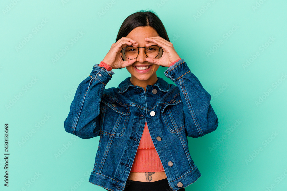 Young mixed race woman isolated on blue background showing okay sign over eyes Young mixed race woman isolated on blue background showing okay sign over eyes