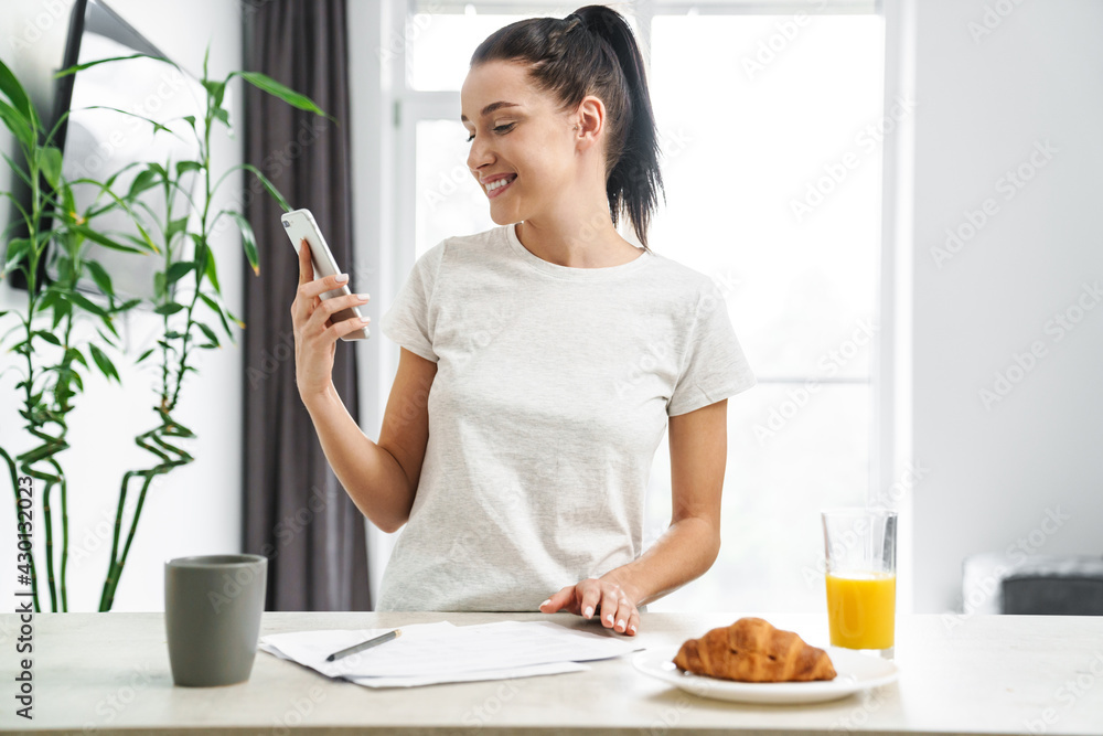 European smiling woman using mobile phone while having breakfast