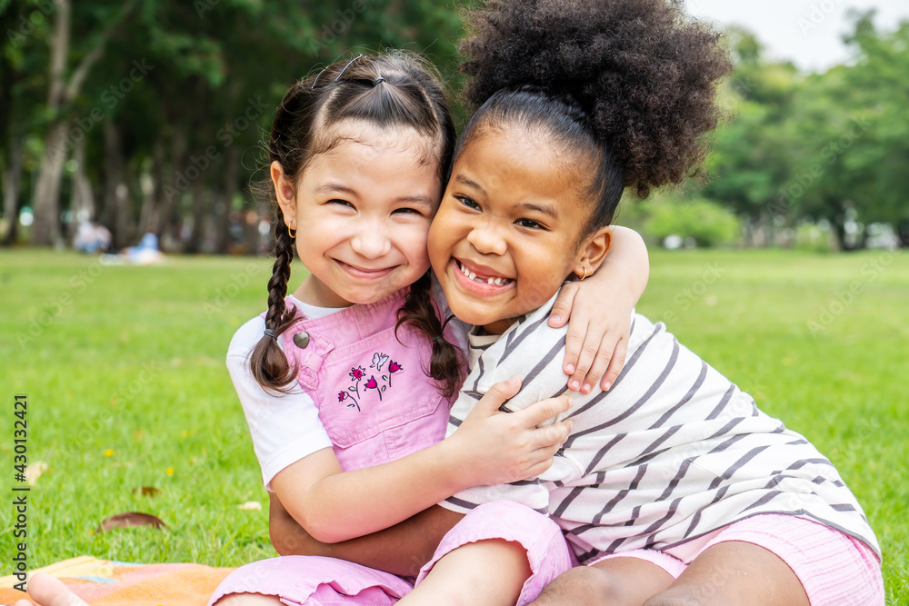 Two African American cheerful little girl sitting on the mat and hugging each other with love in the garden Two African American cheerful little girl sitting on the mat and hugging each other with love in the garden