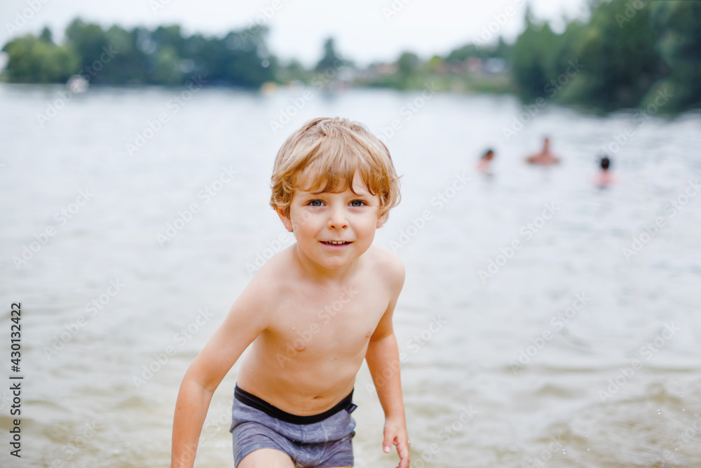 Little blond preschool boy having fun with splashing in a lake on summer day, outdoors. Happy child learning swimming. Active leisure with kids on vacations. Danger on domestic lakes Little blond preschool boy having fun with splashing in a lake on summer day, outdoors. Happy child learning swimming. Active leisure with kids on vacations. Danger on domestic lakes