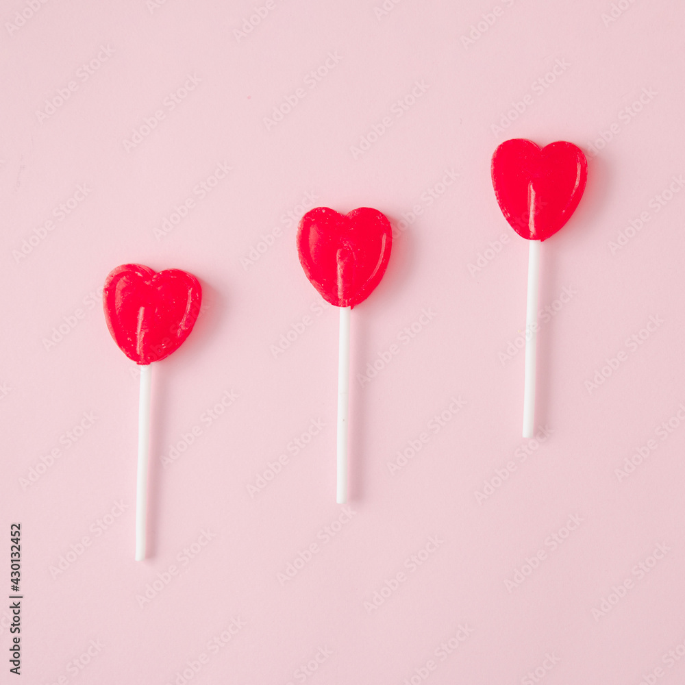 Hearth shaped lollipops on a pastel pink background. Minimal aesthetic.