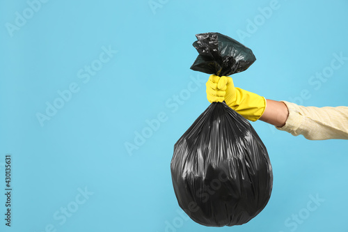 Woman holding full garbage bag on light blue background, closeup. Space for text photo