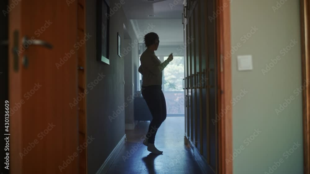 Happy Young Woman Wearing Headphones Dances Through Her Apartment Hallway. Following Shot of Cheerful Girl Listening Music in a Good Mood. Happy Young Woman Wearing Headphones Dances Through Her Apartment Hallway. Following Shot of Cheerful Girl Listening Music in a Good Mood.