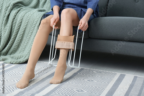 Woman wearing compression tights with donner on sofa indoors, closeup. Space for text
