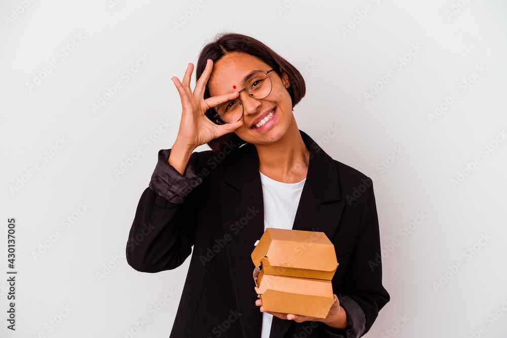 Young business indian woman eating burgers isolated excited keeping ok gesture on eye. Young business indian woman eating burgers isolated excited keeping ok gesture on eye.