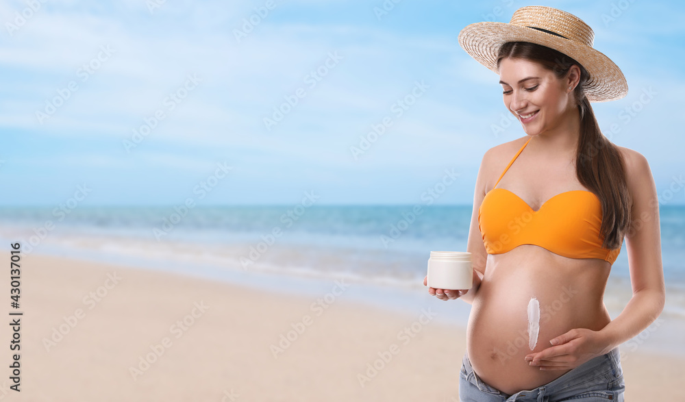 Young pregnant woman with sun protection cream on beach. Space for text