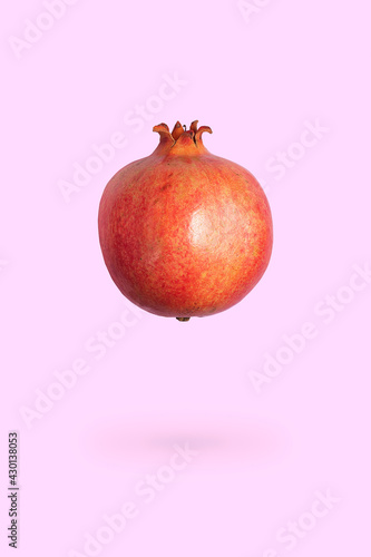 Levitating food. Ripe whole pomegranate floating in the air on pink background