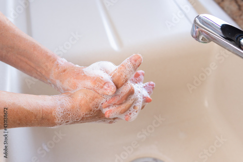Elderly woman washing her hands with soap in a kitchen sink under a faucet. Concept of personal hygiene for ncov corona virus (covid-19) infection prevention or general healthcare. Close-up.
