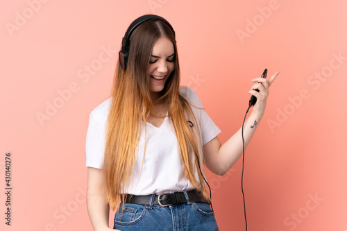 Young caucasian woman isolated on pink background listening music and doing guitar gesture