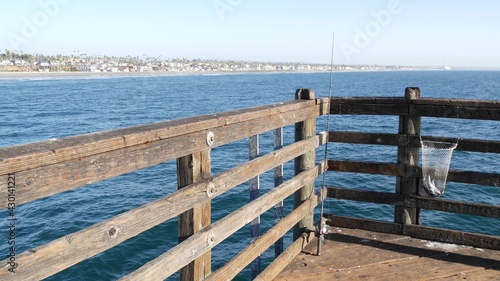 Saltwater angling  wooden pier boardwalk  fishing accessory  tackle or gear. Oceanside California USA. Sea salt water  ocean seascape. Rod or spinning  fisherman catch  fresh alive fish in net basket.