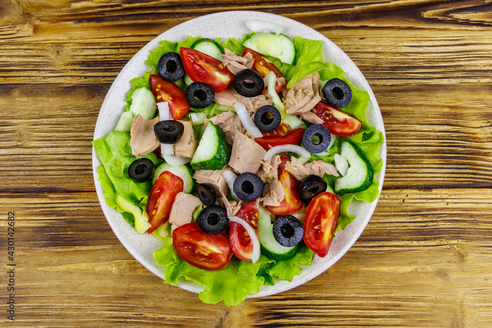Tasty tuna salad with lettuce, black olives and fresh vegetables on wooden table. Top view