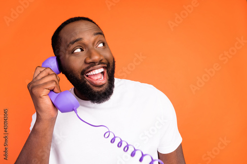 Photo of cheerful happy afro american young man look empty space speak telephone isolated on orange color background photo