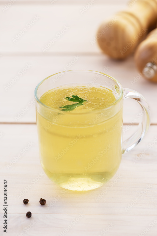 Chicken bone broth with parsley in a glass cup on a wooden table. Chicken bone broth with parsley in a glass cup on a wooden table.