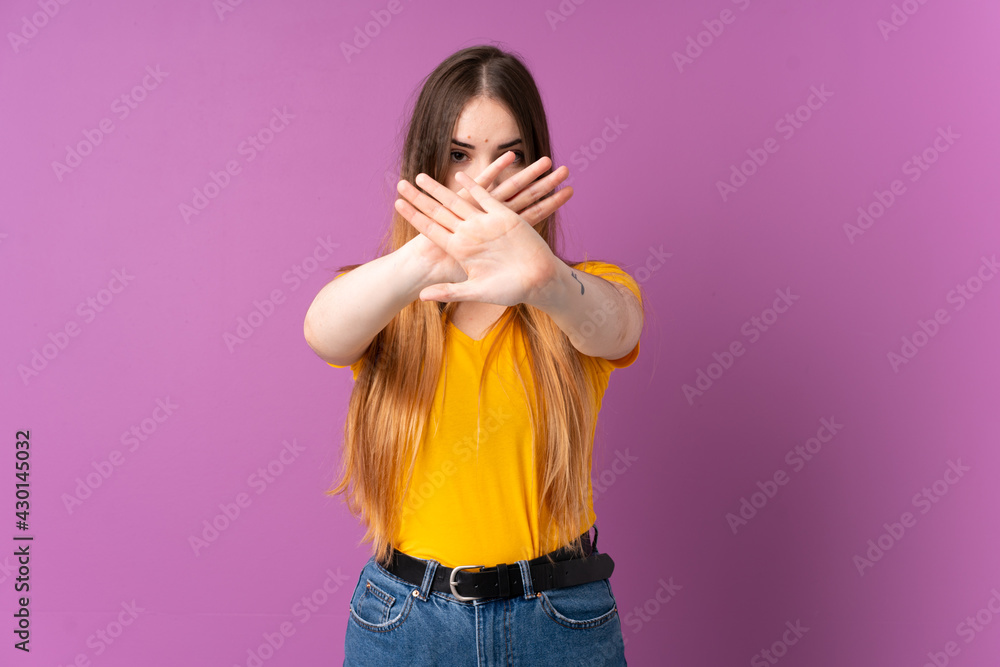 Young caucasian woman isolated on purple background making stop gesture with her hand to stop an act Young caucasian woman isolated on purple background making stop gesture with her hand to stop an act