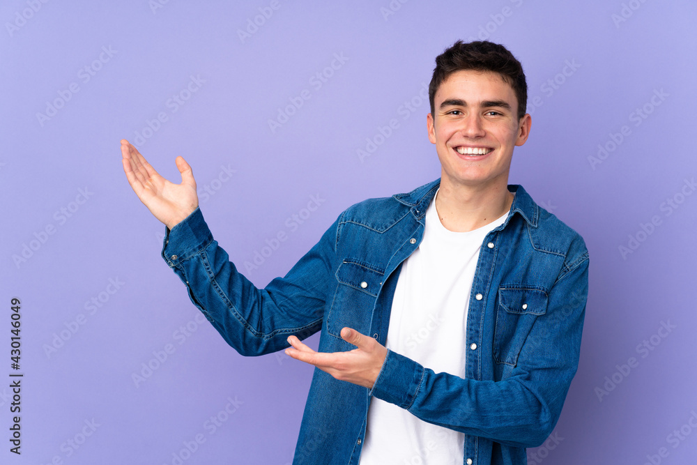 Teenager caucasian handsome man isolated on purple background extending hands to the side for inviting to come Teenager caucasian handsome man isolated on purple background extending hands to the side for inviting to come