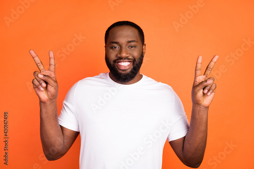 Photo of happy cheerful young dark skin man show v-signs good mood cool isolated on orange color background