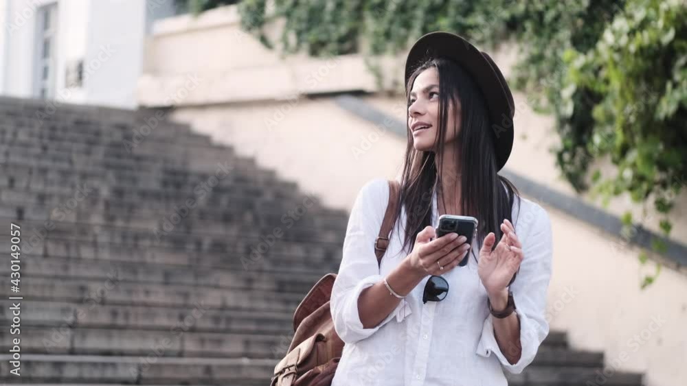 A beautiful young woman is trying to find something using her smartphone while walking outside in summer A beautiful young woman is trying to find something using her smartphone while walking outside in summer