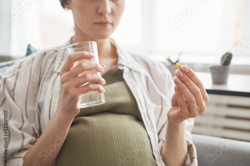 Close-up of pregnant woman holding glass with water and drinking vitamins in the morning