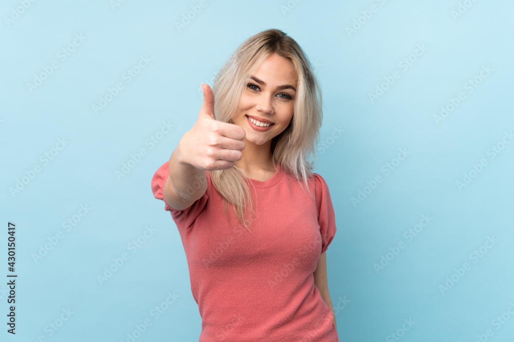 Teenager girl over isolated blue background with thumbs up because something good has happened Teenager girl over isolated blue background with thumbs up because something good has happened