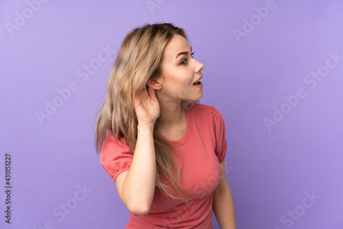 Teenager Russian girl isolated on purple background listening to something by putting hand on the ear © luismolinero