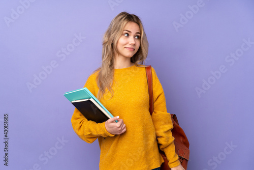 Teenager Russian student girl isolated on purple background making doubts gesture looking side