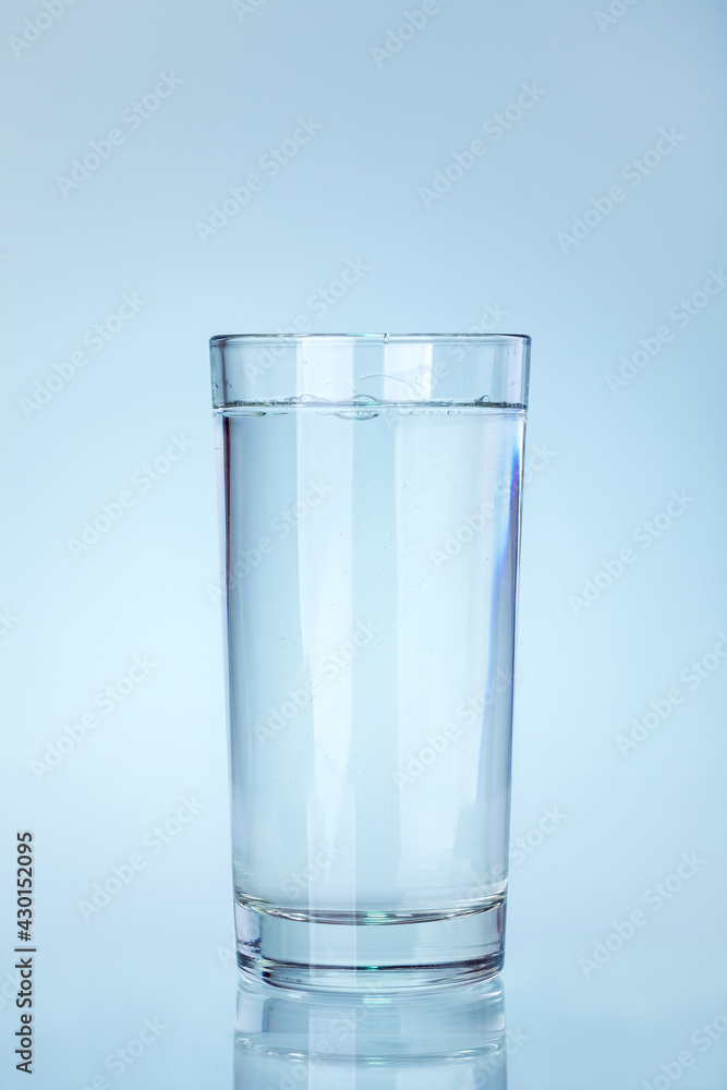clear glass beaker filled with water with a reflection on a cold blue background a water utensil item, nobody. clear glass beaker filled with water with a reflection on a cold blue background a water utensil item, nobody.