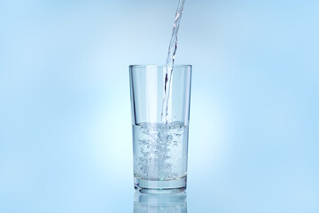 transparent glass is filled with water from a stream of liquid stream, drinkware on a blue background with copy space.