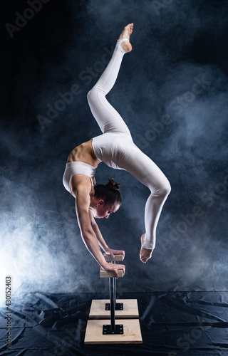 Fototapeta Flexible circus artist - female acrobat doing handstand on the back and smoker background