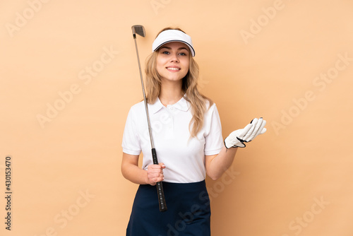 Teenager Russian girl isolated on beige background playing golf and doing coming gesture