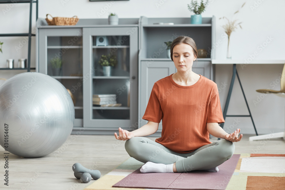 Pregnant woman sitting on exercise mat in lotus position and meditating with eyes closed in the room at home Pregnant woman sitting on exercise mat in lotus position and meditating with eyes closed in the room at home