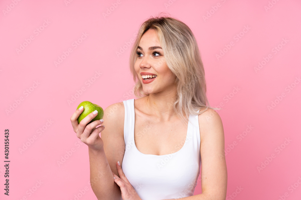 Teenager blonde girl over isolated pink background with an apple and happy Teenager blonde girl over isolated pink background with an apple and happy