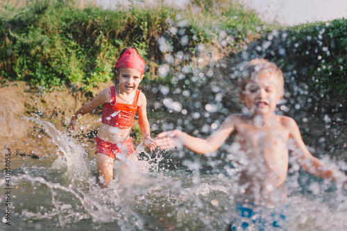 Fototapeta Naklejka Na Ścianę i Meble -  Happy summertime, healthy childhood concept. Caucasian children playing, splashing, jumping and having fun in a river in summer. Selective focus on one kid. Horizontal shot.